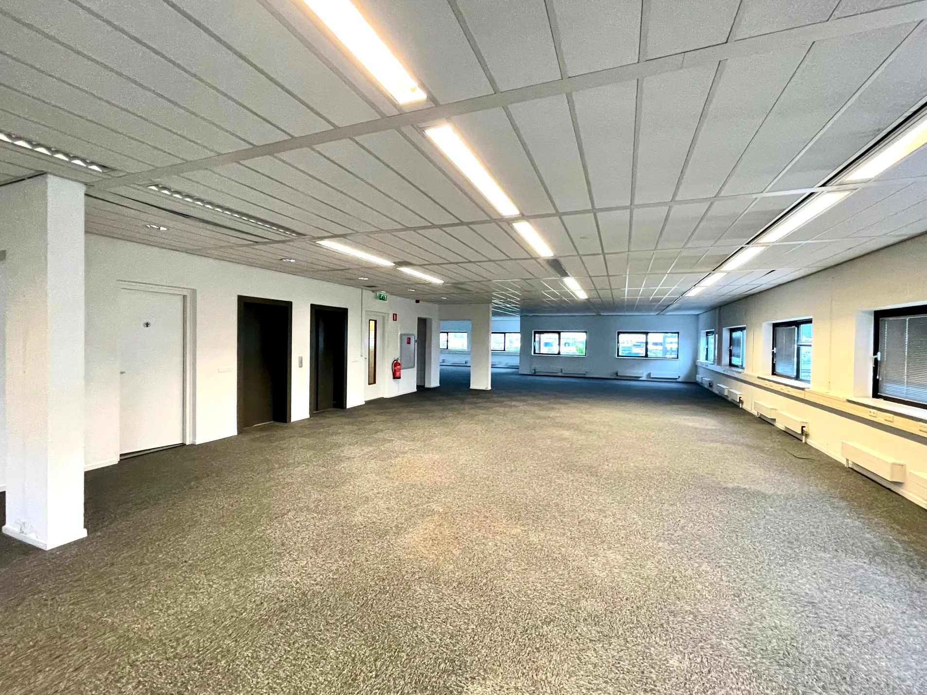 Lichte, ruime kantoorruimte aan de Karel Doormanweg met grijze vloerbedekking en meerdere ramen.